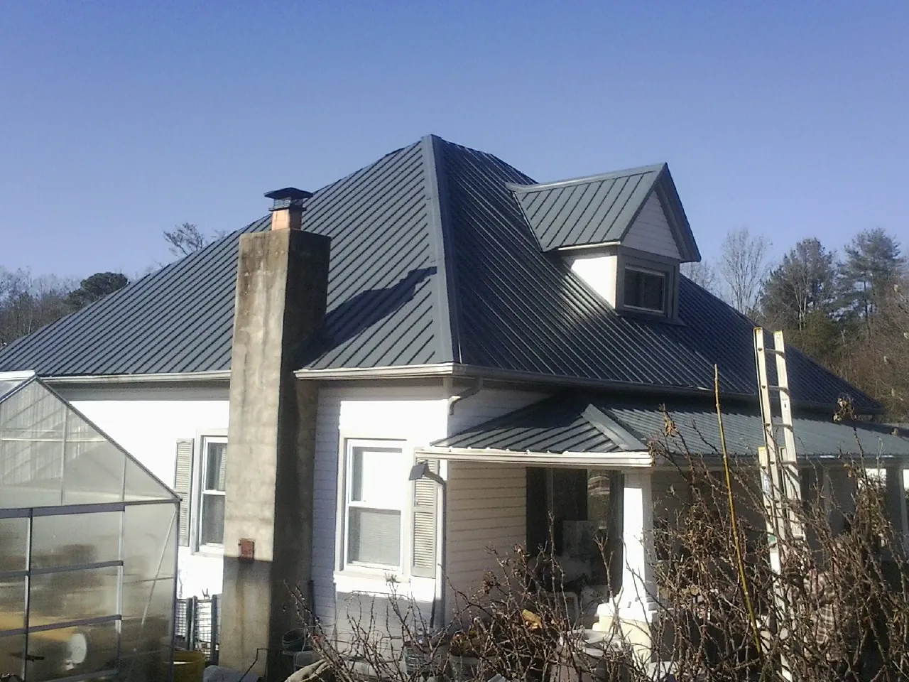 Dark blue standing seam metal roof on a white farmhouse with dormer — Slate & Tile Roof Repair by Roofing Brothers in Broadalbin