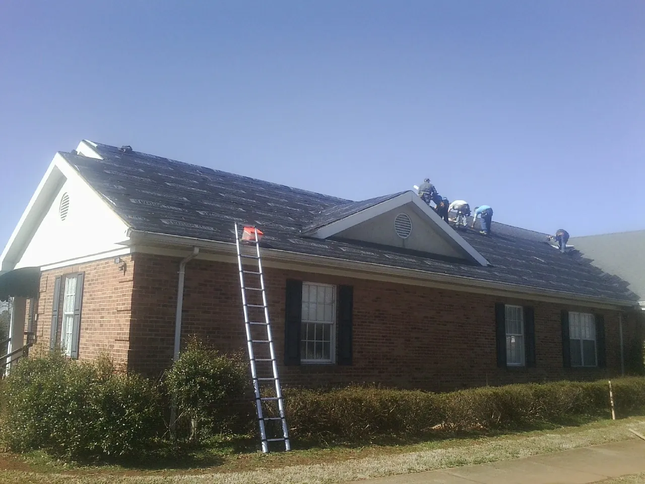 Crew tearing shingles off a brick ranch roof with a ladder set — Emergency Roof Repair work by our crew in Broadalbin