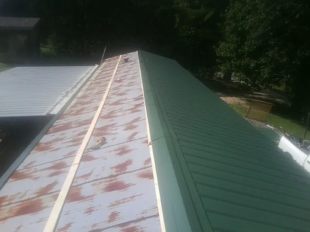 Old rusted panels beside newly installed green metal roofing — Wind Damage Roof Repair by Roofing Brothers in Broadalbin