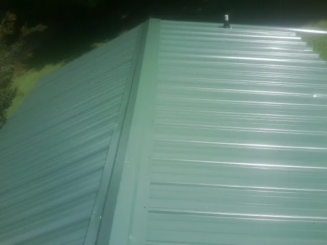 New green metal panels meeting at the ridge of a roof — Flat Roof Repair work by our crew in Broadalbin