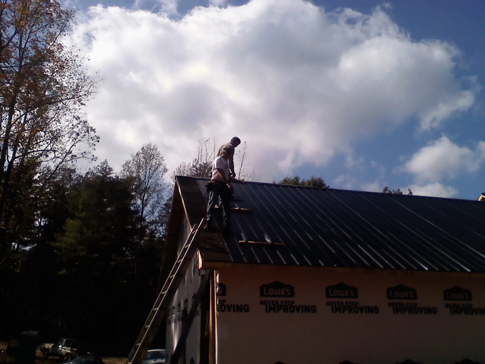 Roofer fastening dark metal panels high against a cloudy sky, from a Roof Inspection job in Broadalbin